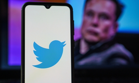Twitter logo on smartphone and Elon Musk in the background. Elon Musk joins Twitter board