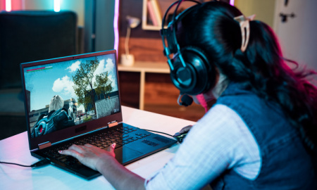 Shoulder shot of woman with headphones playing online video game on laptop at home - concept of live streaming, competitive and technology.